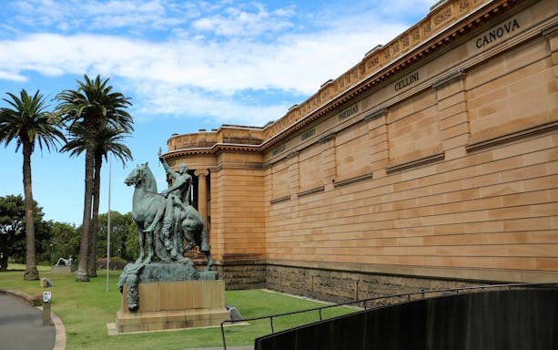 Statue outside Art Gallery of New South Wales, Sydney, with palm trees and classical architecture.