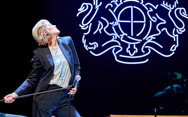 Performer on stage during Inter Alia show on Broadway with neon backdrop.