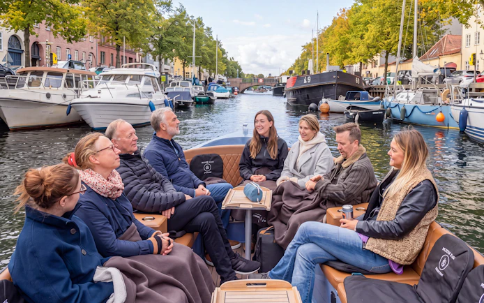 Group enjoying a canal tour in Copenhagen from Ved Stranden, surrounded by boats and greenery.