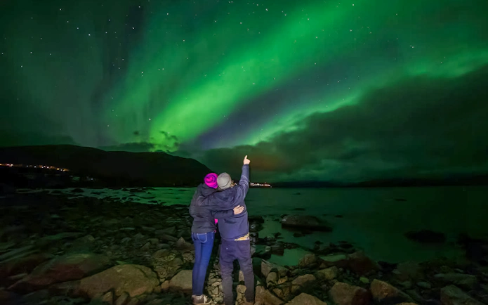 Couple watching northern lights over Lake Torneträsk, Abisko.