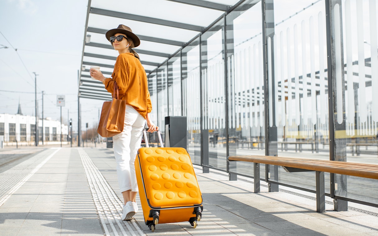 Young female traveler with orange luggage at a modern tram station.
