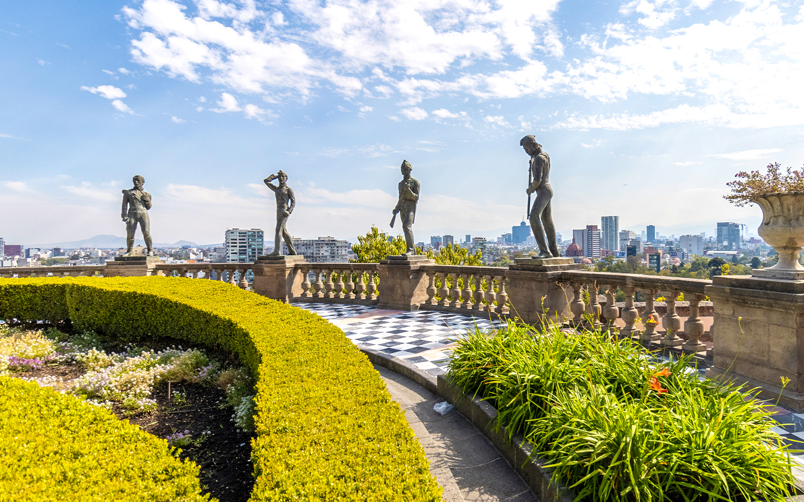 Chapultepec Castle terrace with historic statues overlooking Mexico City skyline.