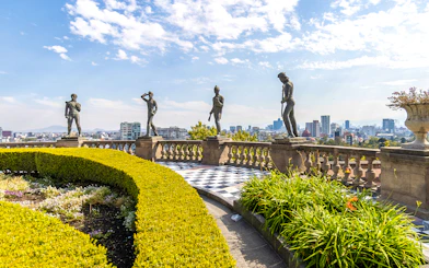 Chapultepec Castle terrace with historic statues overlooking Mexico City skyline.