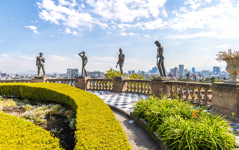 Chapultepec Castle terrace with historic statues overlooking Mexico City skyline.