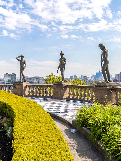 Chapultepec Castle terrace with historic statues overlooking Mexico City skyline.