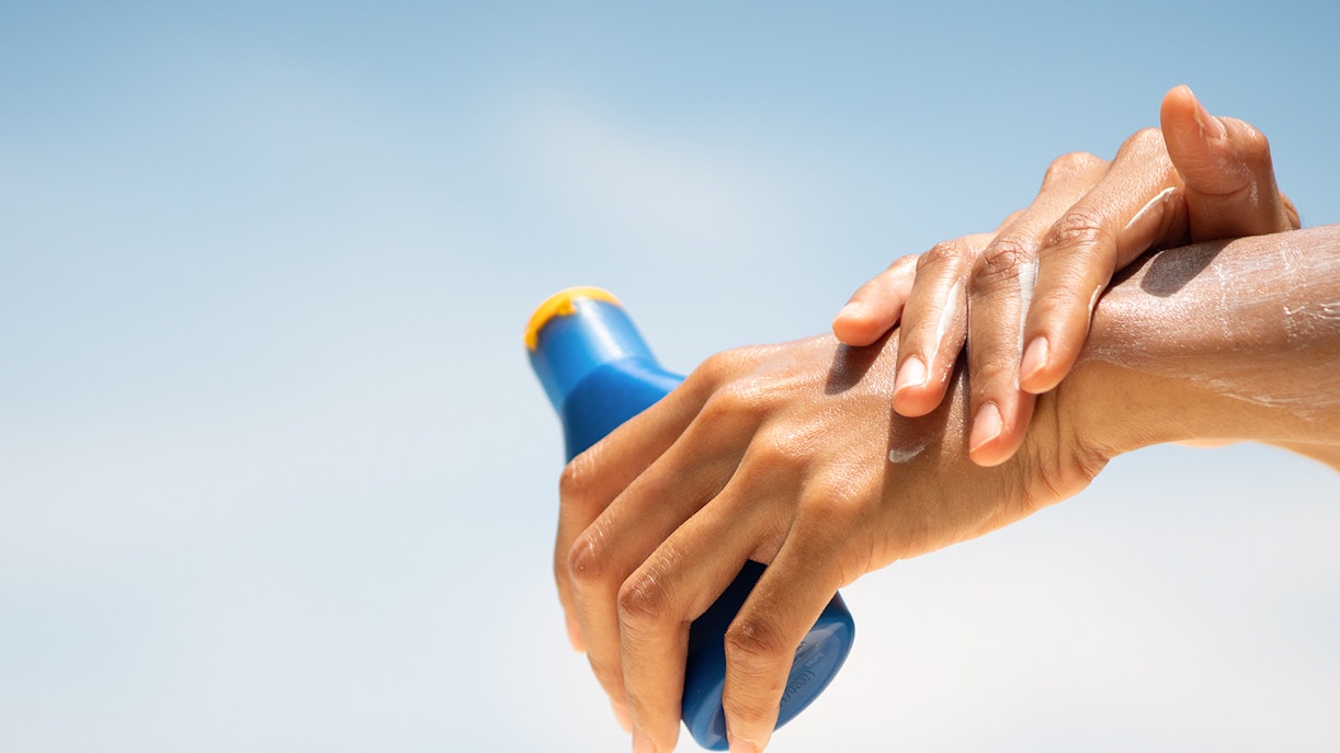Applying sunscreen under a clear blue sky.