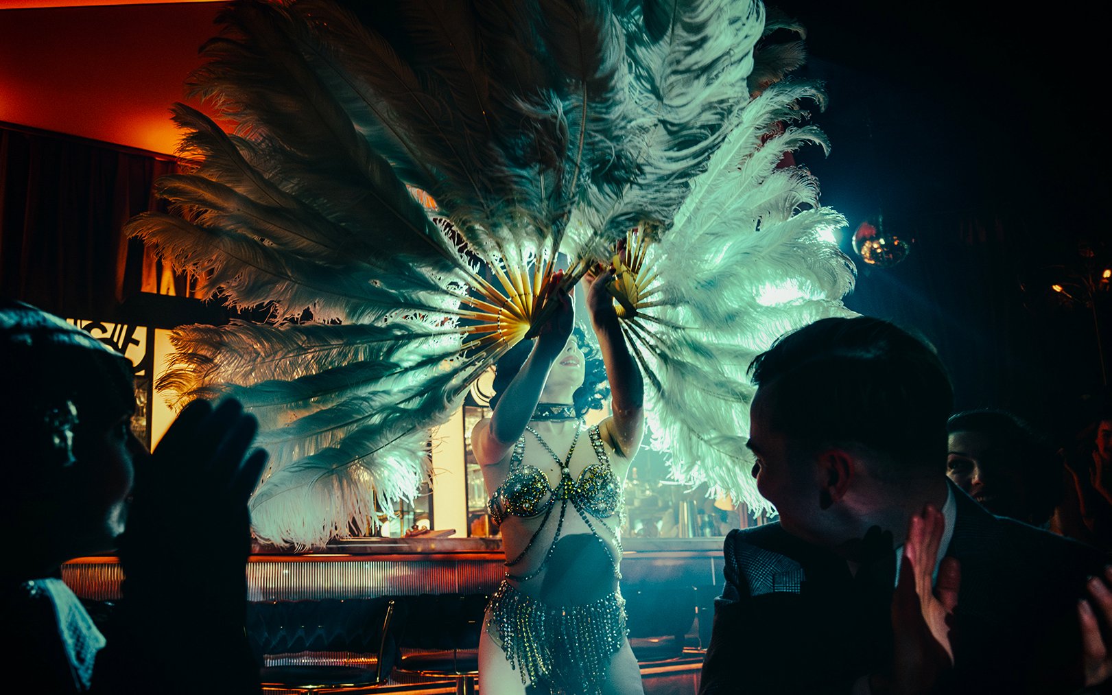 Performer with feather fans on 58th Street stage, audience clapping.