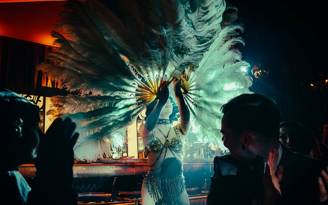 Performer with feather fans on 58th Street stage, audience clapping.