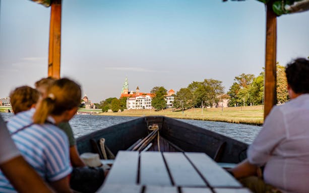 Krakow river cruise on a gondola with view of Wawel Castle in the distance.