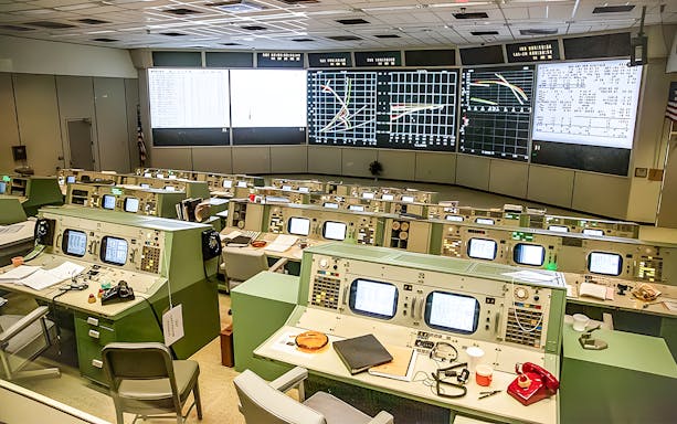 Houston Space Center Control Room with vintage consoles and monitors displaying mission data.