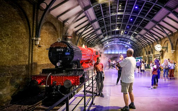Tourists taking photos in front of the Hogwarts Express at a themed attraction.