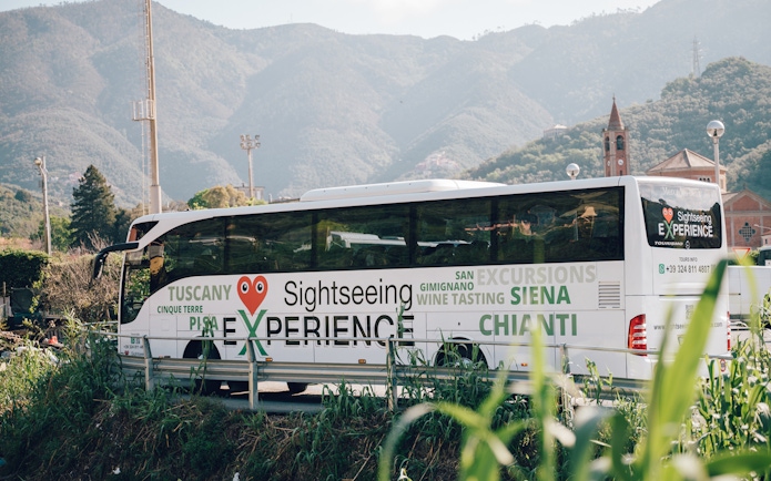 Sightseeing bus in Cinque Terre with mountain backdrop, promoting Tuscany and Siena tours.