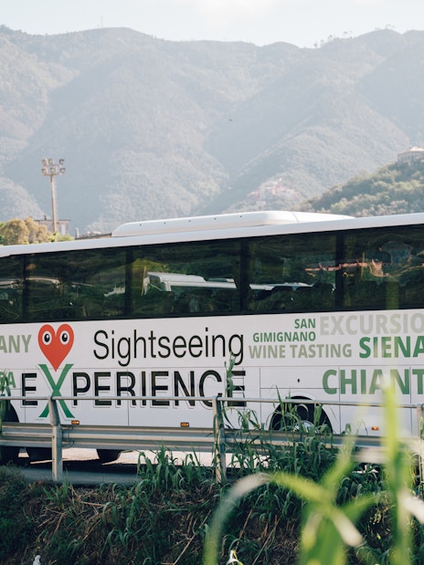 Sightseeing bus in Cinque Terre with mountain backdrop, promoting Tuscany and Siena tours.