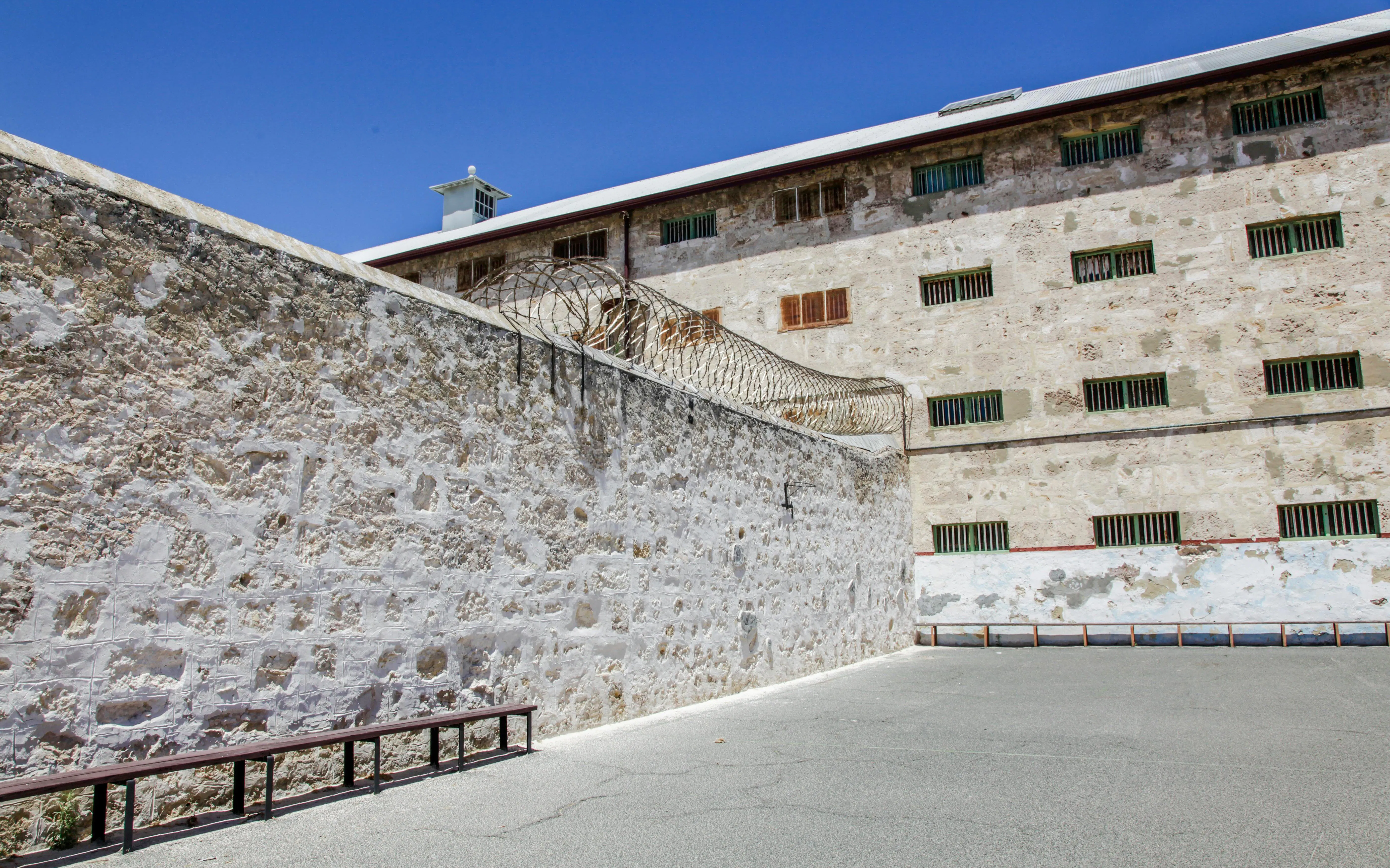 Fremantle Prison courtyard with high stone walls and barbed wire.