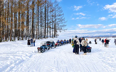 Snowmobiles and visitors at Chiyoda Snow Park, Hokkaido, with trees and mountains in the background.