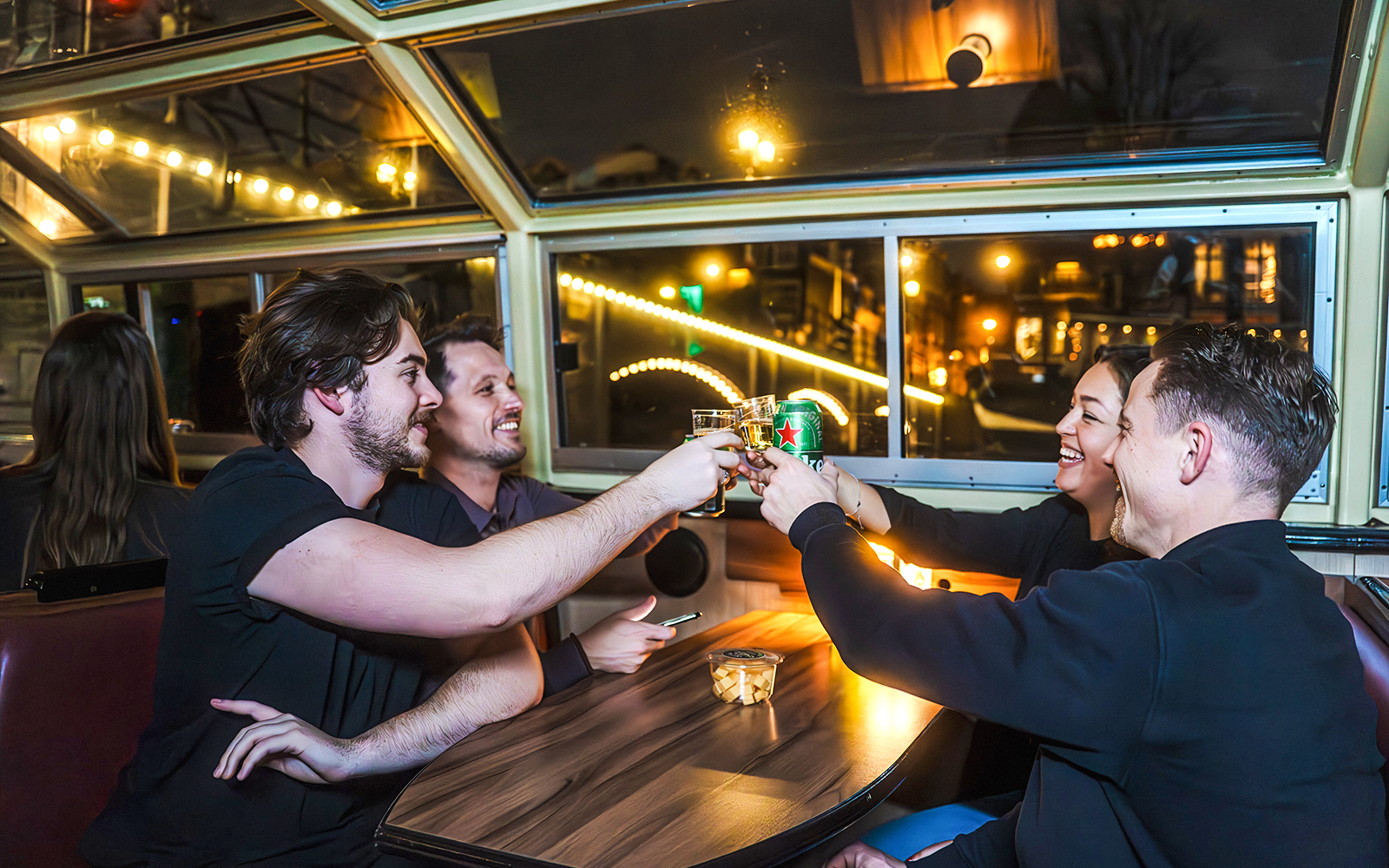 Friends toasting drinks on Amsterdam Light Festival canal cruise.