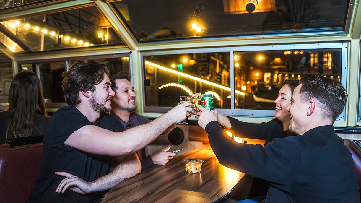 Friends toasting drinks on Amsterdam Light Festival canal cruise.