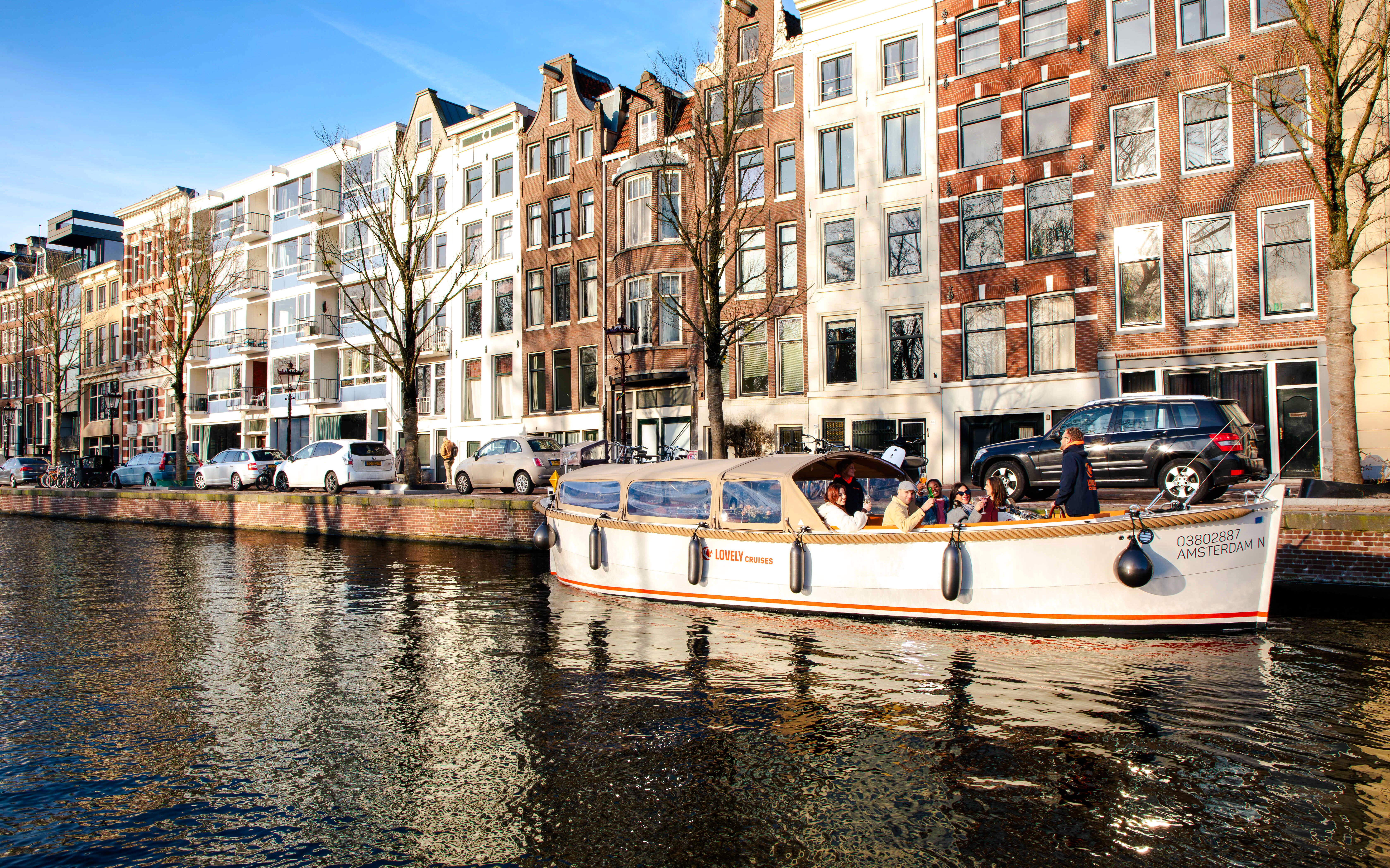 Open boat cruise on Amsterdam canal with historic buildings in the background.