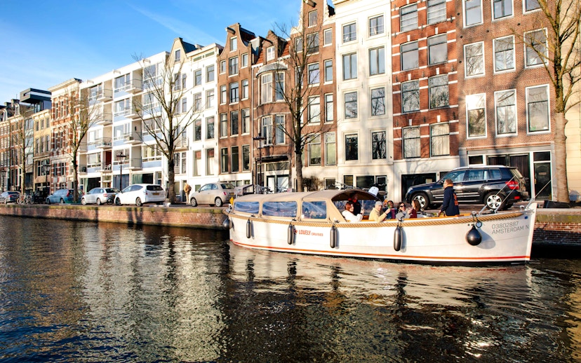 Open boat cruise on Amsterdam canal with historic buildings in the background.