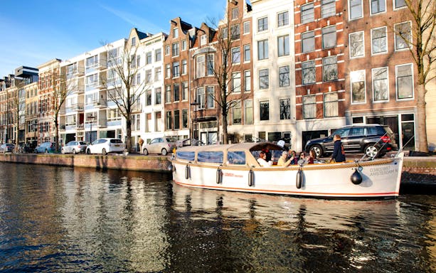 Open boat cruise on Amsterdam canal with historic buildings in the background.