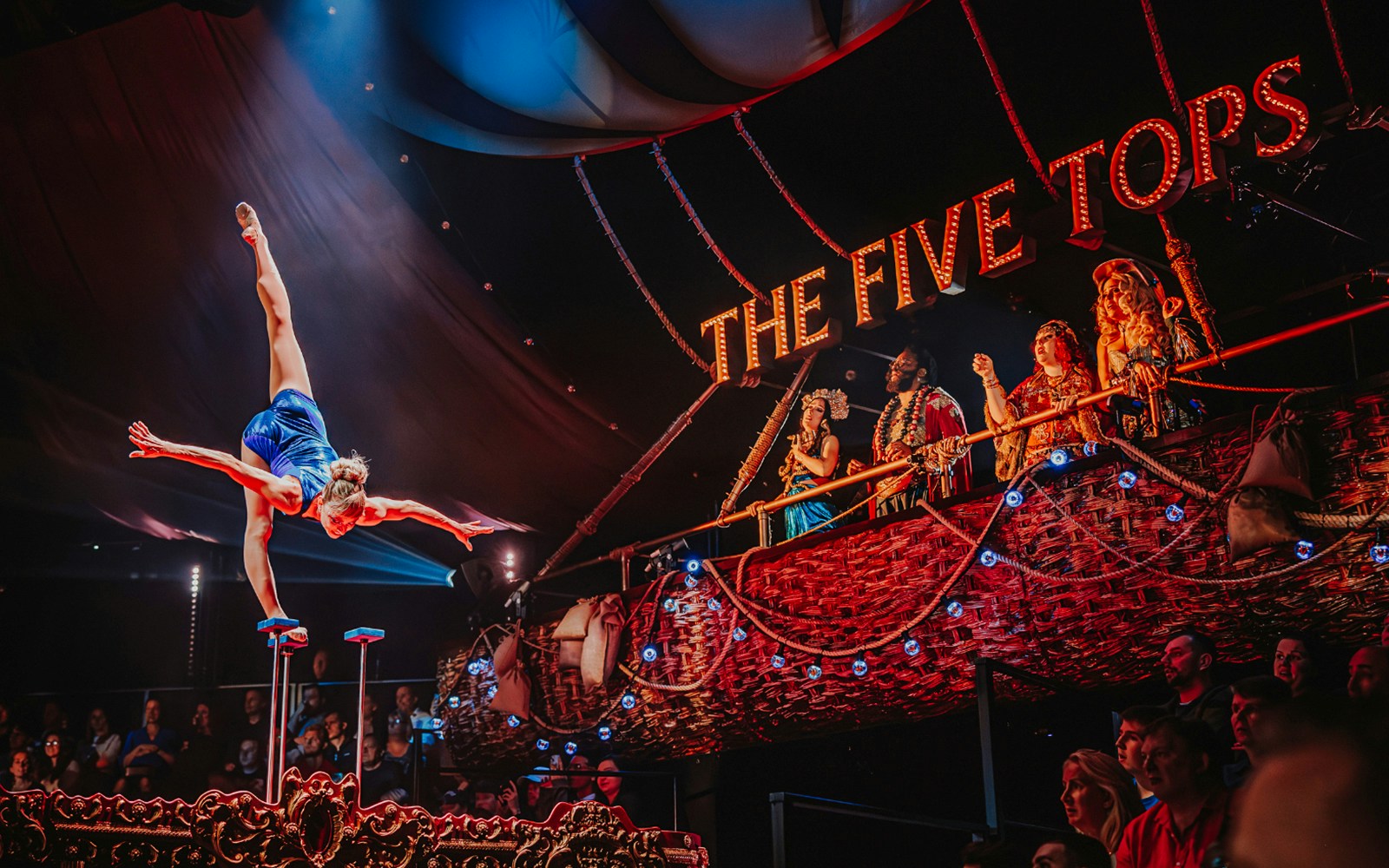 Acrobat performing handstand at The Five Tops show, vibrant audience in background.