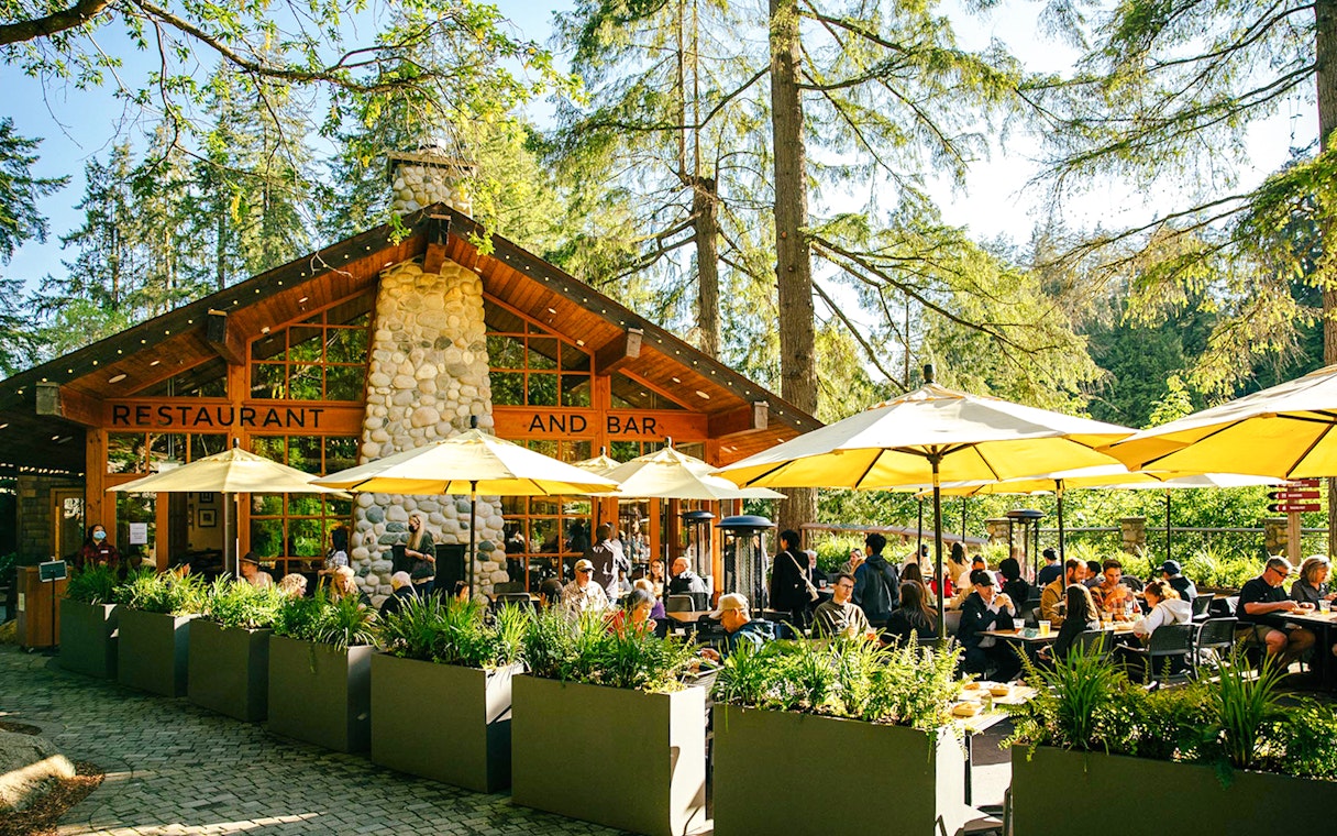 Outdoor dining area at Capilano Suspension Bridge Park with people enjoying meals under yellow umbrellas.