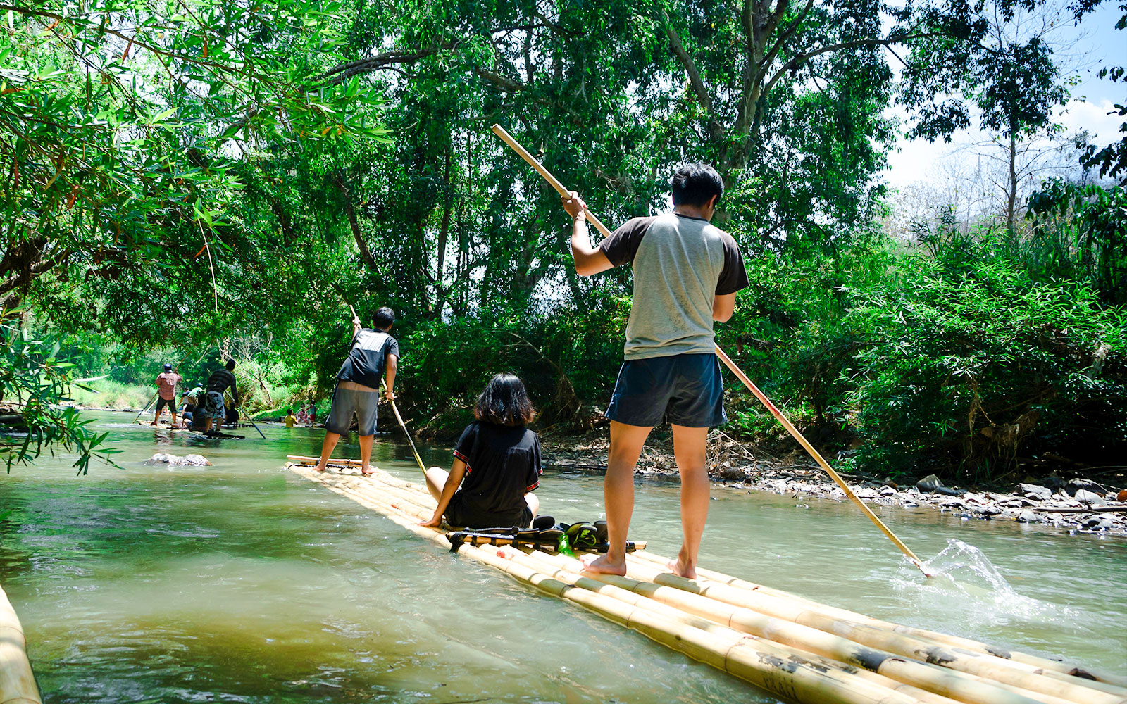 People bamboo rafting on a river surrounded by lush greenery.