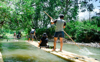 People bamboo rafting on a river surrounded by lush greenery.