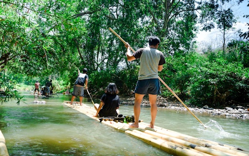 People bamboo rafting on a river surrounded by lush greenery.
