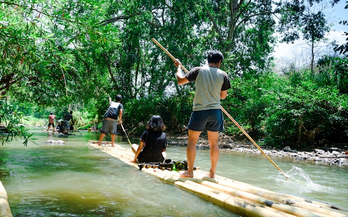 People bamboo rafting on a river surrounded by lush greenery.