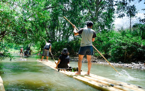 People bamboo rafting on a river surrounded by lush greenery.