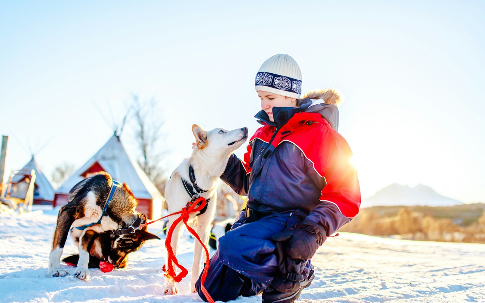 Teenage boy kneeling in snow with husky dog, traditional tents in background.