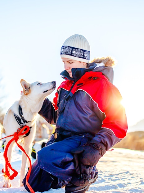 Teenage boy kneeling in snow with husky dog, traditional tents in background.