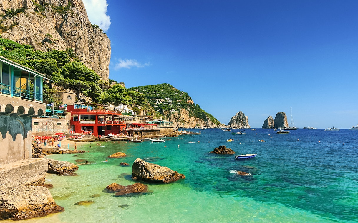 Capri coastline with Faraglioni rocks and boats, part of all-inclusive tour from Pompeii or Naples.