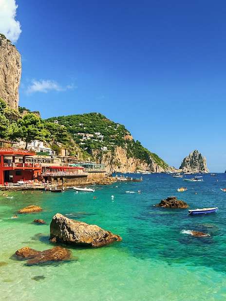 Capri coastline with Faraglioni rocks and boats, part of all-inclusive tour from Pompeii or Naples.