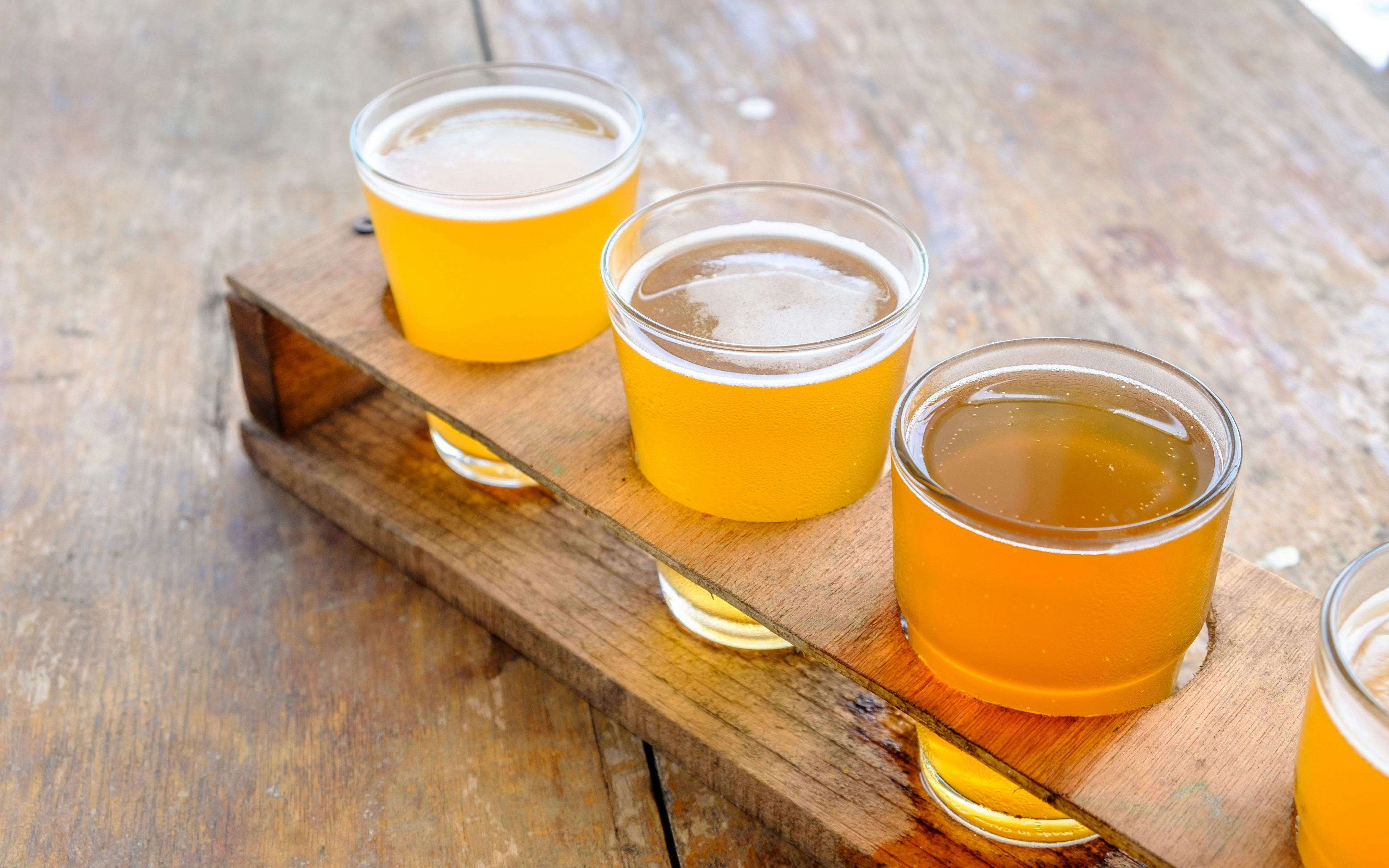 Craft beer and cider flight on a wooden tray for tasting experience.
