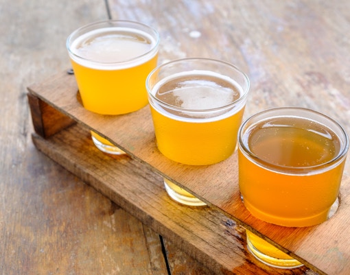 Craft beer and cider flight on a wooden tray for tasting experience.