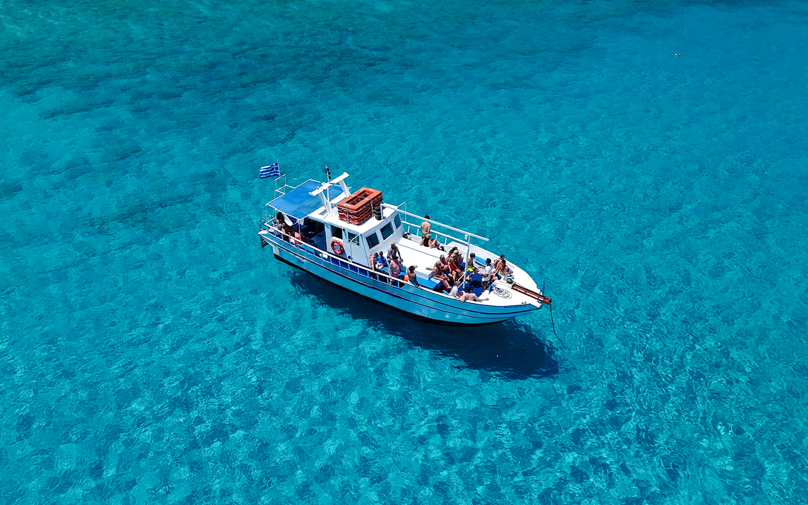 Boat with tourists on Lindos cruise over turquoise sea water.
