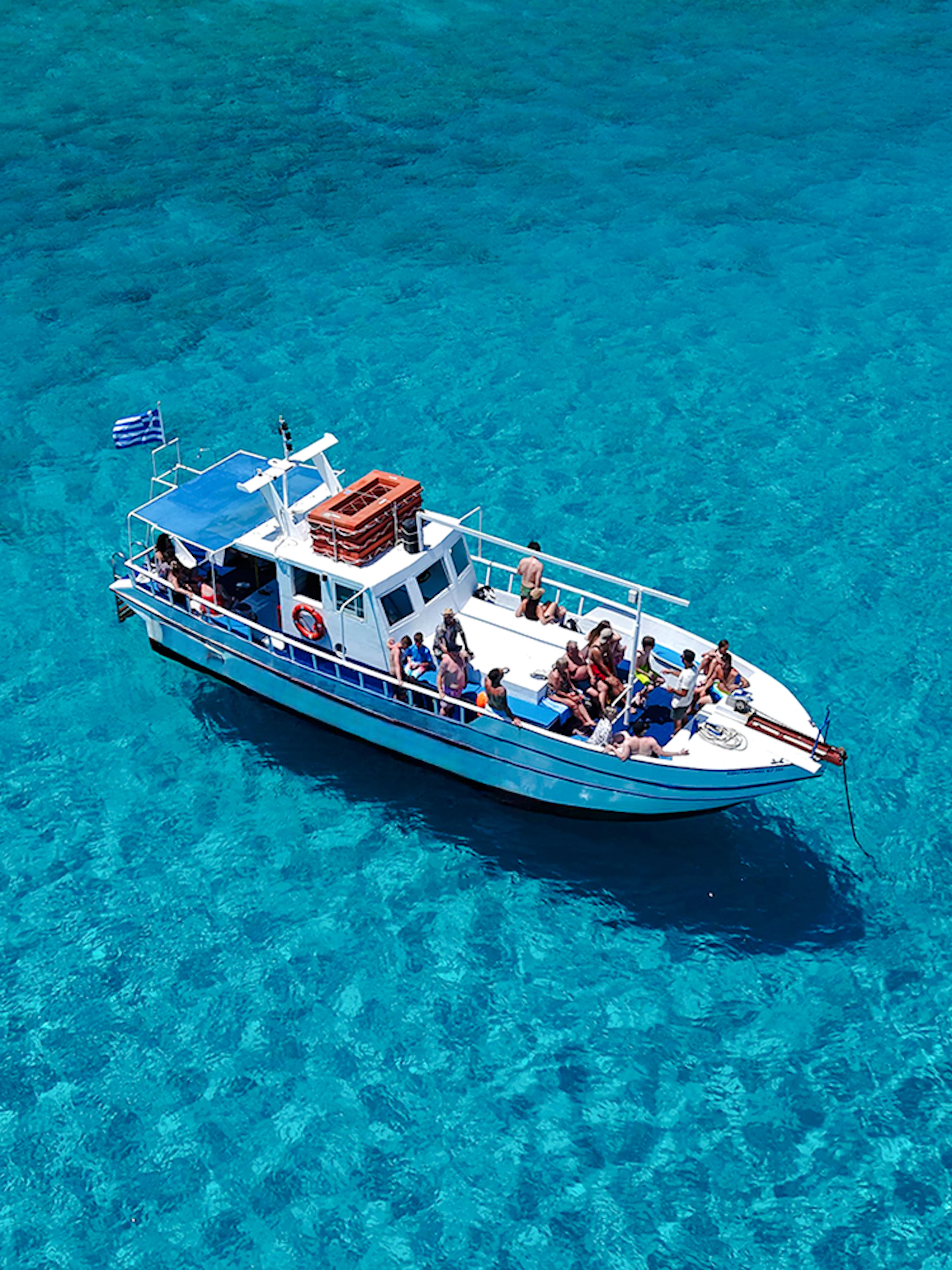 Boat with tourists on Lindos cruise over turquoise sea water.