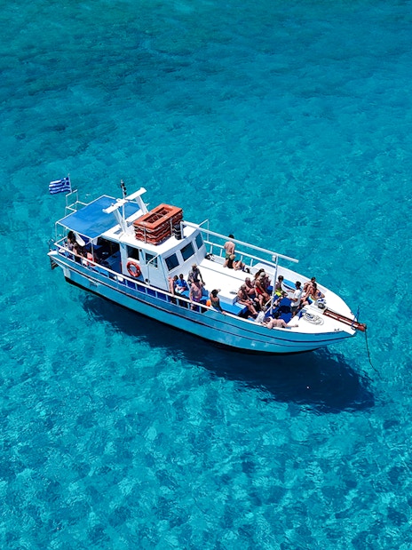 Boat with tourists on Lindos cruise over turquoise sea water.