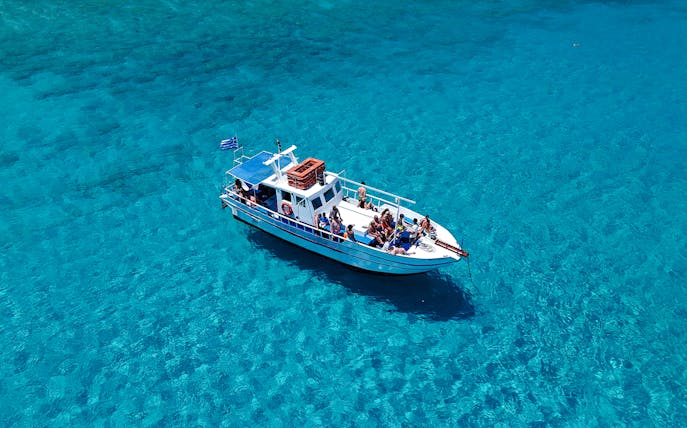 Boat with tourists on Lindos cruise over turquoise sea water.
