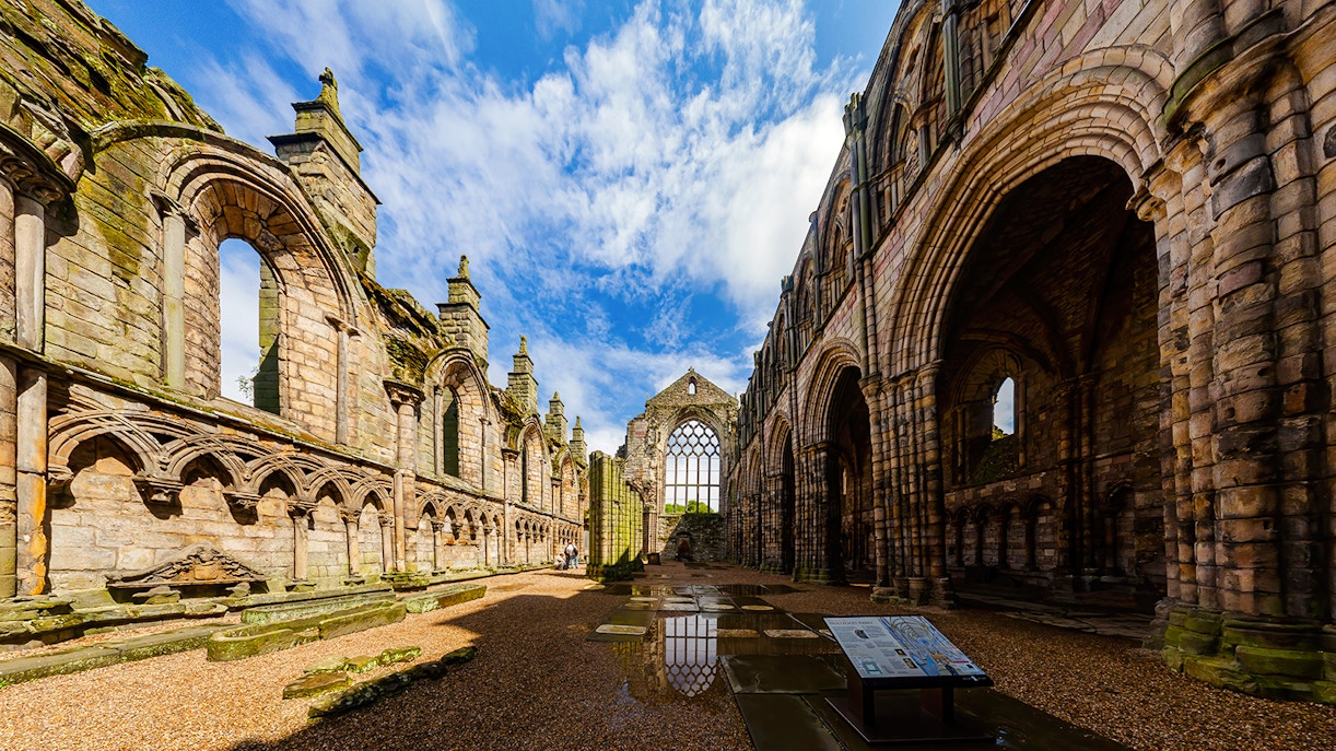 Ruins of Holyrood Abbey with stone arches and blue sky in Edinburgh, Scotland.