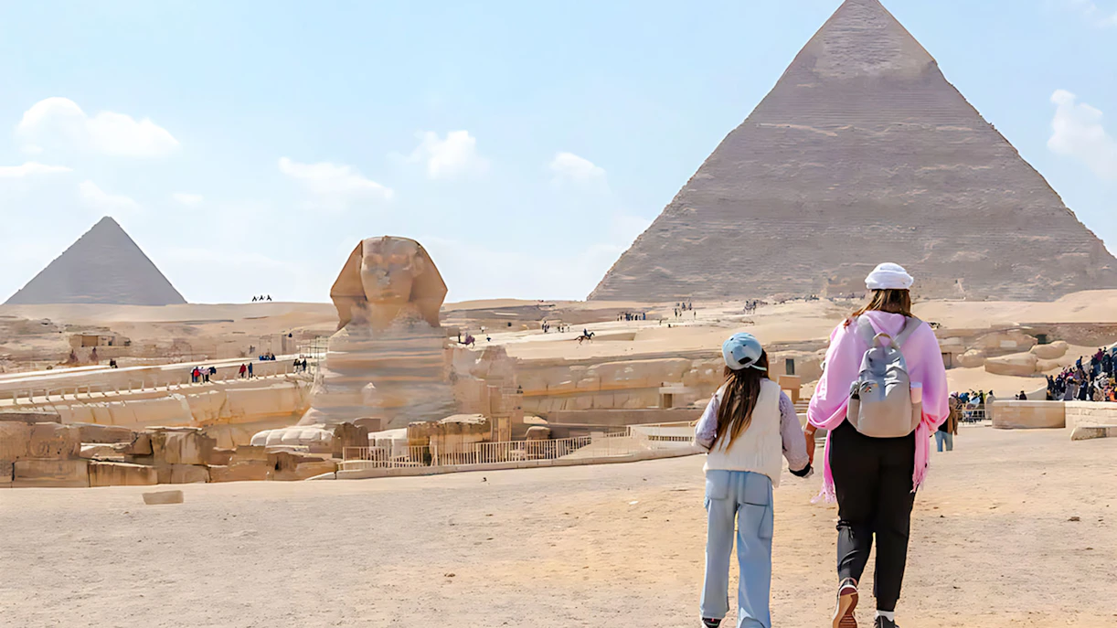 Mother and child walking towards the Pyramid of Giza and Sphinx in Egypt.
