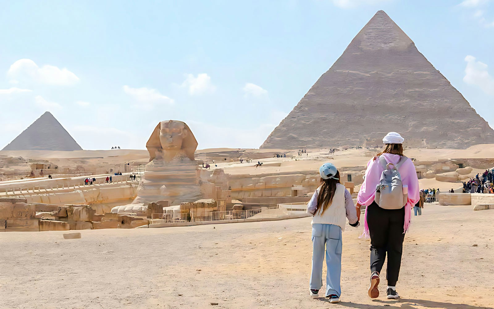Mother and child walking towards the Pyramid of Giza and Sphinx in Egypt.
