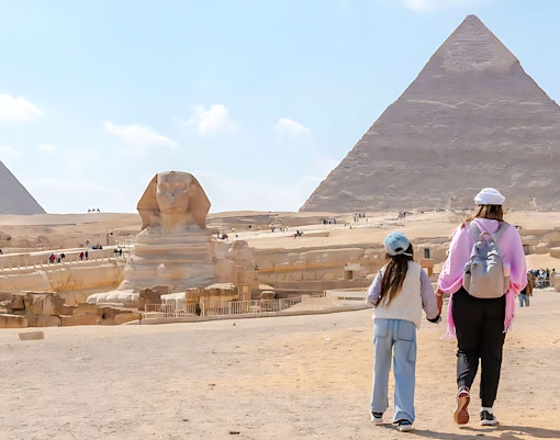 Mother and child walking towards the Pyramid of Giza and Sphinx in Egypt.