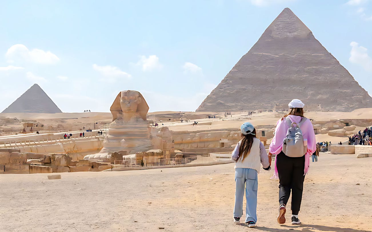 Mother and child walking towards the Pyramid of Giza and Sphinx in Egypt.