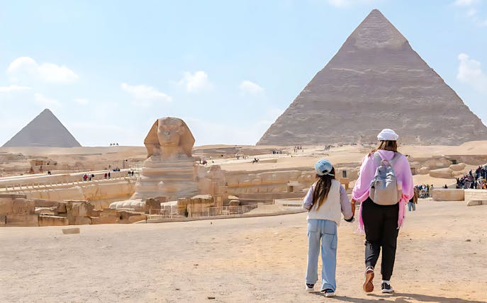 Mother and child walking towards the Pyramid of Giza and Sphinx in Egypt.