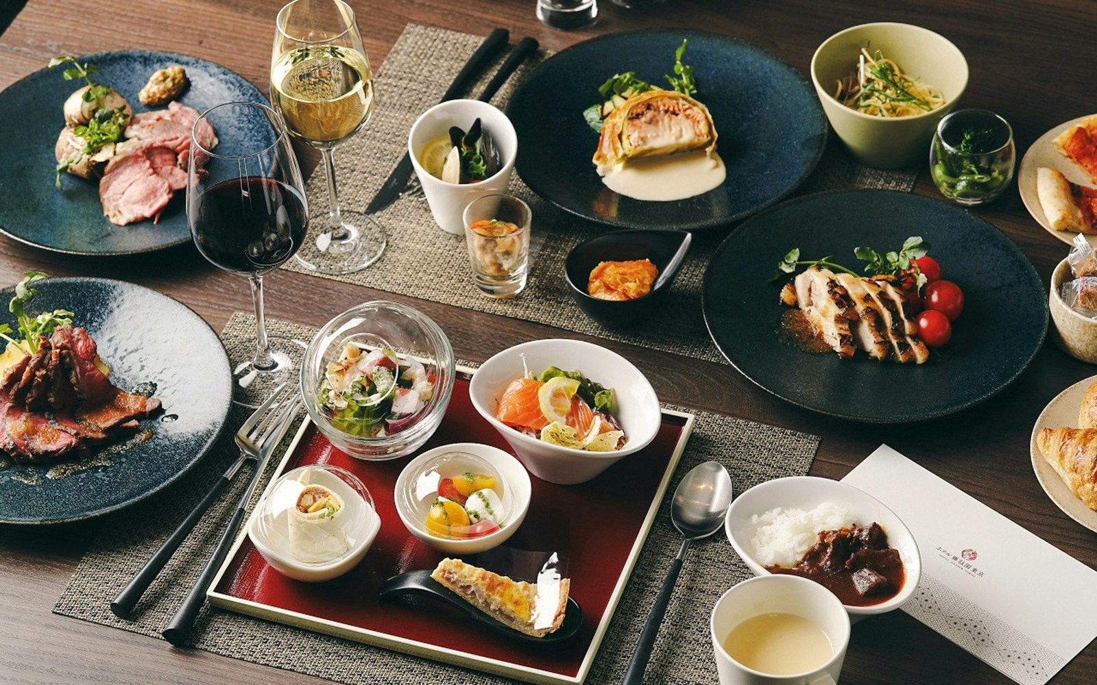 Assorted dishes at Ghibli Museum restaurant, including sushi, salad, and wine.