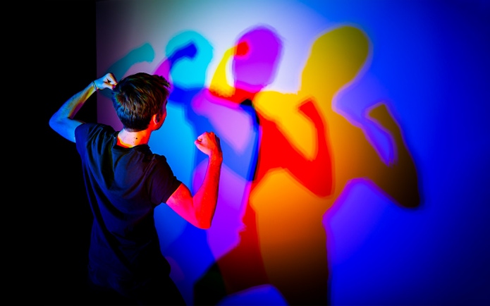 Person interacting with colorful shadows at Museo de las Ilusiones Sevilla.