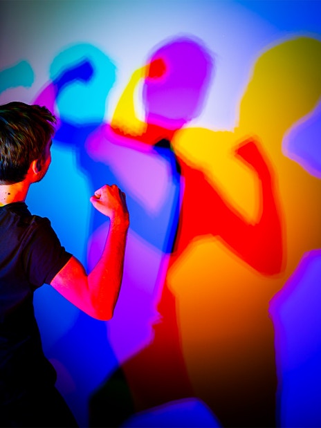 Person interacting with colorful shadows at Museo de las Ilusiones Sevilla.